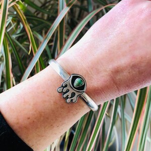 May include: A silver bracelet with a green turquoise stone set in a silver paw print design.
