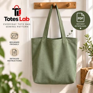 Puede incluir: Un bolso tote de lona color verde salvia con dos correas largas para el hombro, colgado de un gancho de madera. La imagen incluye el texto: Totes Lab, Everyday Tote Bag Sewing Pattern, Beginner Friendly, Detailed Instructions y PDF Instant Download.