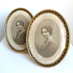 Puede incluir: Dos marcos de fotos ovalados con bordes dorados y detalles decorativos negros. Cada marco contiene una fotografía de retrato vintage en tono sepia de una persona con el pelo corto, vistiendo una prenda con cuello, protegida por cristal curvo.