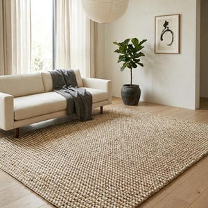 May include: A large rectangular area rug featuring a thick, chunky knit texture in a neutral beige and cream color palette. The rug is crafted with a dense, looped weave pattern that creates a tactile, raised surface across the entire floor covering.