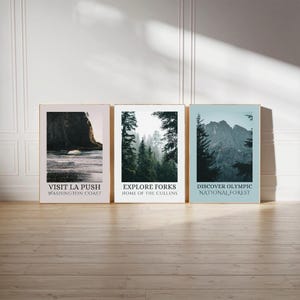 May include: Three framed landscape prints with text. The first print says "VISIT LA PUSH WASHINGTON COAST" with a coastal image. The second print says "EXPLORE FORKS HOME OF THE CULLENS" with a forest image. The third print says "DISCOVER OLYMPIC NATIONAL FOREST" with a mountain image.