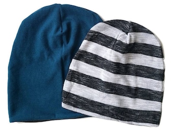 Può includere: Due berretti sono mostrati su sfondo bianco. Uno è di colore verde acqua unito, l'altro presenta strisce orizzontali bianche e nere. I berretti sono realizzati in morbido materiale a maglia, adatti all'uso casual.