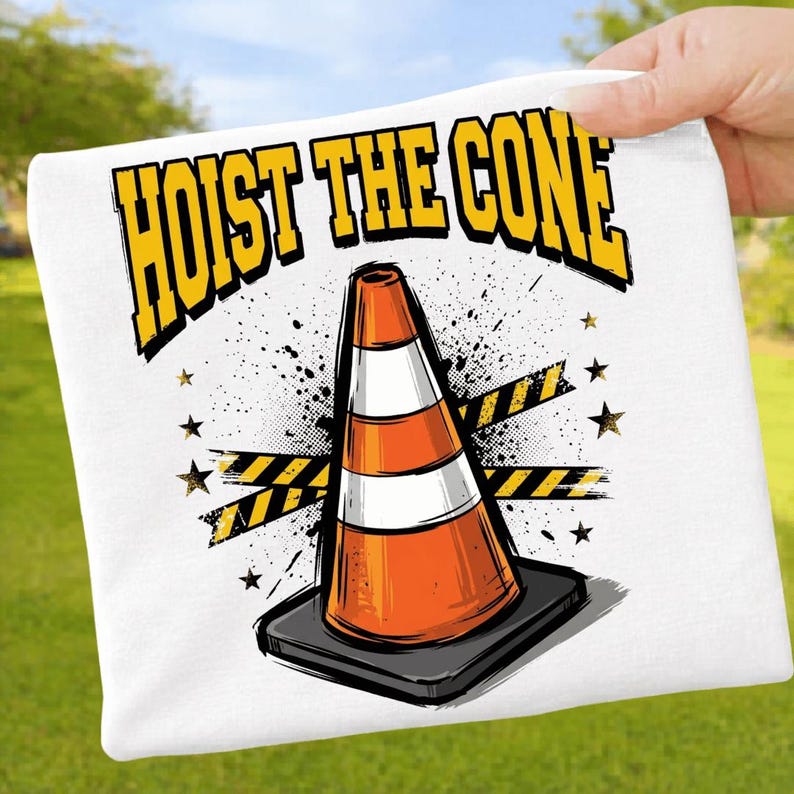 Puede incluir: Camiseta blanca con un gr&aacute;fico de un cono de tr&aacute;fico naranja y blanco. El texto "HOIST THE CONE" es amarillo. El dise&ntilde;o incluye salpicaduras negras, estrellas amarillas y cinta de precauci&oacute;n.