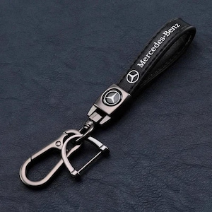 Peut inclure: Porte-clés Mercedes-Benz en cuir noir avec un mousqueton en métal argenté. Le porte-clés présente le logo et la marque Mercedes-Benz en blanc. La conception comprend un mousqueton robuste pour fixer les clés.