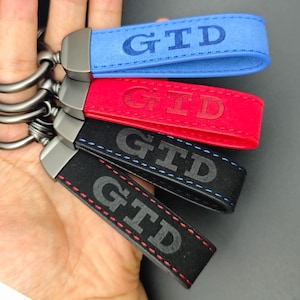 Könnte beinhalten: Eine Sammlung von Schlüsselanhängern in Blau, Rot und Schwarz. Jeder Schlüsselanhänger hat die Buchstaben "GTD" auf dem Riemen geprägt. Die Schlüsselanhänger sind an einem silbernen Metallring befestigt.