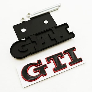 May include: Black GTI emblem with red trim, a black mounting plate, and hardware. The emblem is a car accessory, likely for a Volkswagen. The GTI logo is displayed on a white background.