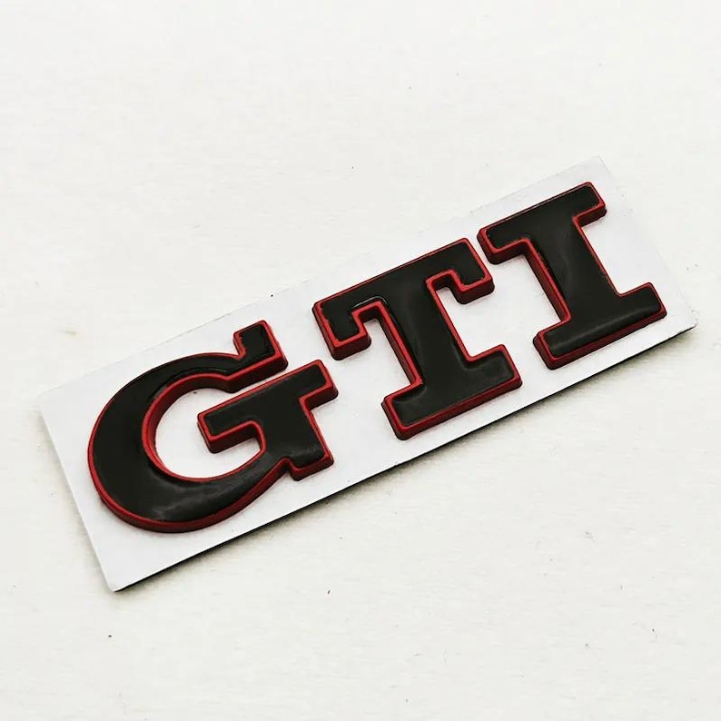 May include: Black and red GTI badge on a white background. The letters are black with a red border, giving a 3D appearance. This emblem is likely for a vehicle, possibly a Volkswagen.
