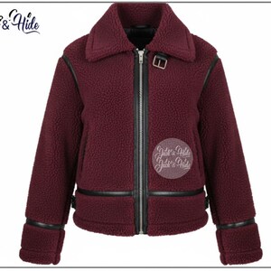 May include: A burgundy fleece jacket with a black zipper, collar, and trim. The jacket has a buckle detail at the collar and cuffs. The brand name "Jack & Hide" is visible in the upper left corner.