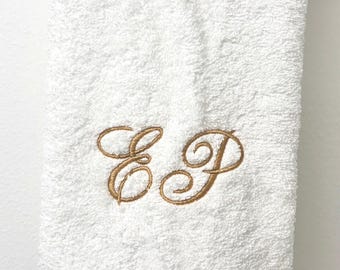 May include: White bath towel with gold embroidered initials "E D". The towel is hanging on a white bar. The towel has a textured surface and a ribbed bottom.