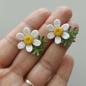 Peut inclure: Une paire de boucles d'oreilles marguerites au crochet. Chaque boucle d'oreille présente une marguerite blanche avec un centre jaune et des feuilles vertes. Ces petites boucles d'oreilles délicates sont parfaites pour ajouter une touche de charme inspirée de la nature.