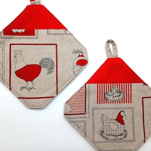 Könnte beinhalten: Zwei gesteppte Topflappen mit Bauernhof-Motiv. Jeder hat eine rote Oberseite und eine rautenförmige Form mit beigem Hintergrund. Einer zeigt einen roten Hahn, der andere ein Huhn in einem Nest. Beide haben eine Schlaufe zum Aufhängen.