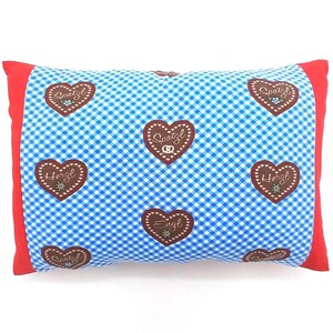Könnte beinhalten: Rechteckiges Kissen mit blau-weißem Karomuster. Es hat braune herzförmige Motive mit den Wörtern "Herzl" und "Spatzl" in weißer Schrift. Die Kanten sind rot.
