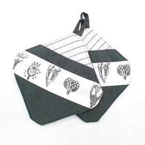 Könnte beinhalten: Zwei schwarz-weiße Topflappen mit botanischem Design. Die Topflappen haben einen schwarzen Rand und einen weißen Streifen mit schwarzen Blumenillustrationen. Die Rückseite der Topflappen hat ein schwarz-weißes Karomuster.