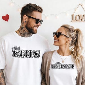 Puede incluir: Dos personas con camisetas blancas con texto negro. Una camiseta dice "KING" en una fuente adornada con una corona, y la otra dice "QUEEN" en un estilo similar. Ambos llevan gafas de sol y sonríen.