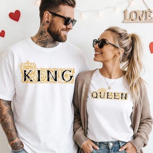 Puede incluir: Camisetas blancas a juego con texto dorado y negro que dice "KING" y "QUEEN". El texto está en una fuente decorativa con una corona encima de la palabra. La pareja lleva gafas de sol y sonríe.