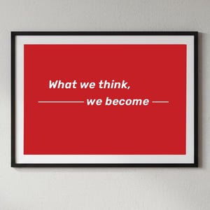May include: Framed art print with a red background and the quote "What we think, we become" in white. The text is centered and underlined. The frame is black.