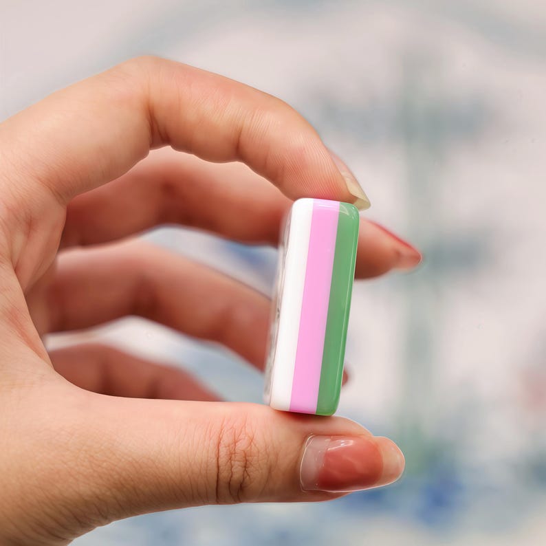 Pode incluir: Um bloco retangular com tr&ecirc;s faixas verticais distintas nas cores branco, rosa claro e verde claro. O objeto possui um acabamento liso e brilhante e espessura uniforme, exibindo um design de camadas coloridas em seu perfil lateral.