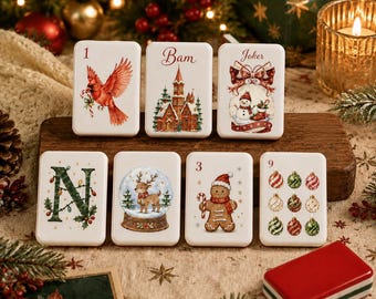 Puede incluir: Un conjunto de siete azulejos rectangulares blancos con ilustraciones navideñas, que incluyen un cardenal, un edificio invernal, un muñeco de nieve, la letra N, un reno en una bola de nieve, un hombre de jengibre y nueve adornos, más una caja roja.
