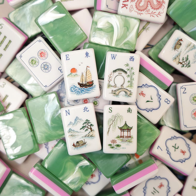 Pode incluir: Uma cole&ccedil;&atilde;o de pe&ccedil;as retangulares de mahjong com faces brancas apresentando ilustra&ccedil;&otilde;es coloridas de paisagens, navios e caracteres chineses, combinadas com versos em m&aacute;rmore verde. As pe&ccedil;as exibem marcadores direcionais, incluindo E, W, N e S.