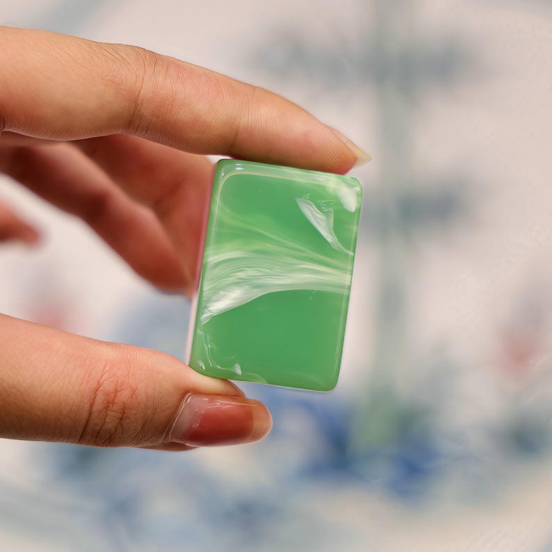 Pode incluir: Uma pe&ccedil;a retangular de resina verde lisa com um padr&atilde;o de m&aacute;rmore branco que se espalha por toda a superf&iacute;cie. O objeto tem cantos arredondados e um acabamento brilhante, exibindo uma apar&ecirc;ncia consistente, s&oacute;lida e opaca.