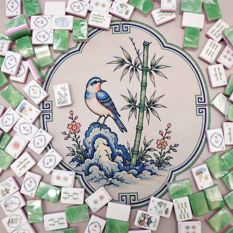 Pode incluir: Um tapete redondo de mahjong com uma ilustra&ccedil;&atilde;o central de um p&aacute;ssaro azul pousado numa rocha ao lado de um caule de bambu e flores cor-de-rosa, rodeado por uma cole&ccedil;&atilde;o dispersa de pe&ccedil;as de mahjong brancas e verdes marmoreadas.