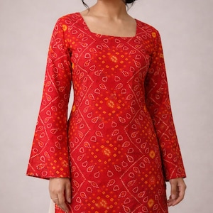 May include: A red tunic with a square neckline and long bell sleeves. The tunic features a repeating pattern of small yellow and white shapes. The garment is part of a traditional Indian style of clothing.