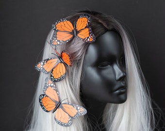 May include: Three orange and black butterfly hair clips on a white wig. The wig is on a black mannequin head.