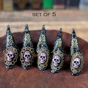 Set of 5 resin skull claw rings displayed on wooden surface.