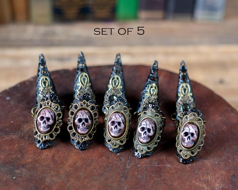 Set of 5 resin skull claw rings displayed on wooden surface.