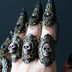 Close-up of resin skull details on gothic pirate nail claws with bronze filigree shown on a woman's hand.