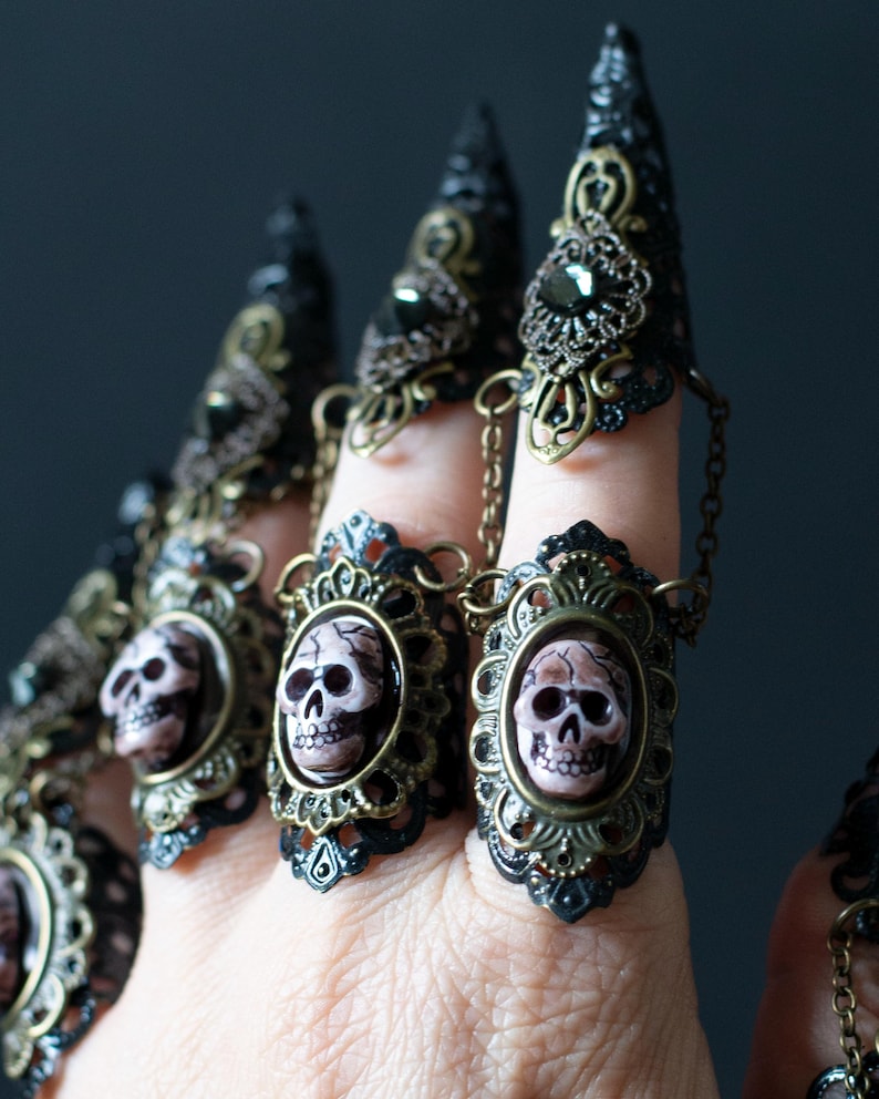 Close-up of resin skull details on gothic pirate nail claws with bronze filigree shown on a woman's hand.