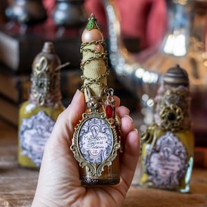 May include: A small glass bottle with a gold and green stopper and a gold chain wrapped around the neck. The bottle is filled with a yellow liquid and has a label that reads "Mad Hatter's Madness Potion".