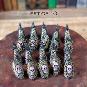 Set of 10 gothic claw rings with skulls displayed on rustic background.