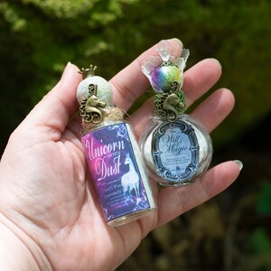 Puede incluir: Dos peque&ntilde;as botellas de vidrio con tapones de corcho y tapas decorativas de metal en forma de unicornio. Las botellas est&aacute;n llenas de polvo blanco y tienen etiquetas que dicen "Unicorn Horn Dust" y "The Will & Magic".