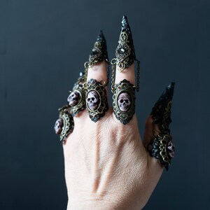 Full hand wearing 5 of the 10-piece gothic mermaid nail claws with resin skulls and filigree details.