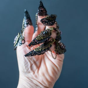 Side view of layered metal filigree and chain draping on skull claw rings.