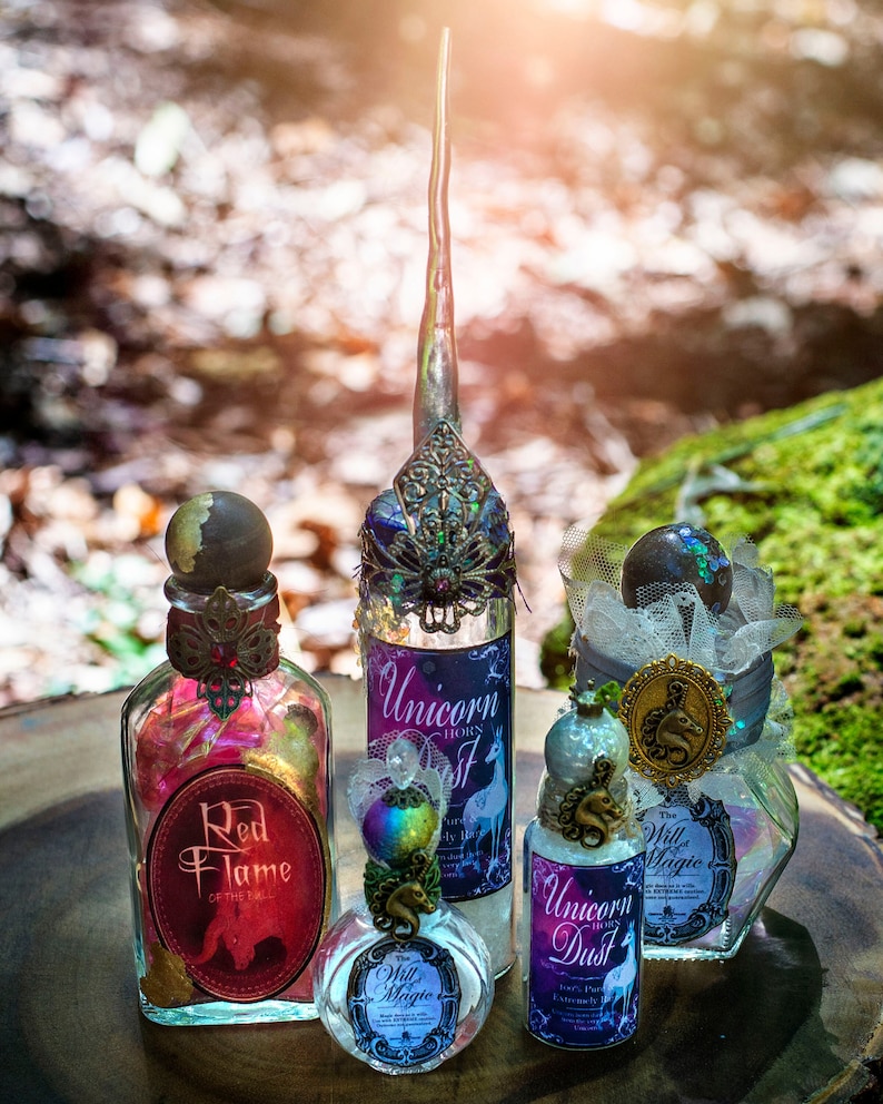 Puede incluir: Tres botellas de vidrio con tapones decorativos y etiquetas. Las botellas contienen l&iacute;quidos coloridos y est&aacute;n decoradas con pan de oro, purpurina y cintas. Las etiquetas dicen "Red Flame", "Unicorn Horns Dust" y "Unicorn Dust".
