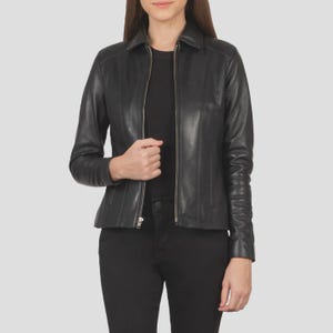 May include: A black leather jacket with a collared neckline and a front zipper closure. The jacket has long sleeves and vertical stitching details on the front. The model is wearing a black top and black pants.