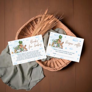 May include: Two baby shower invitation cards with dinosaur and animal illustrations. One card reads "Books for baby" and the other says "Diaper raffle". The cards are on a woven basket with wheat stalks and a sage green cloth.