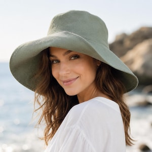 May include: A wide-brimmed sage green sun hat with a rounded crown and a flexible, downward-sloping brim. The hat is constructed from a solid-colored, textured fabric material that provides full coverage for the head and shades the face.