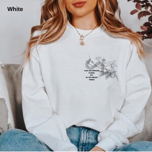 May include: White sweatshirt with a black graphic of a snake and flowers. The text on the sweatshirt reads "Look like innocent flower but be the serpent under". The sweatshirt is a crew neck style.