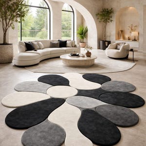 Peut inclure: Salon moderne avec un grand tapis en forme de fleur dans les tons noir, gris et crème. La pièce comprend un canapé incurvé, une table basse ronde et des fenêtres cintrées, créant une atmosphère lumineuse et aérée.