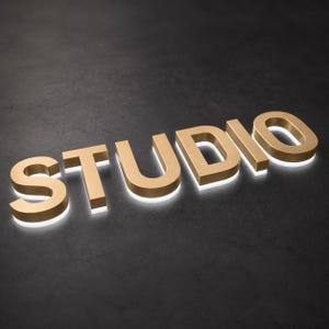 Puede incluir: Un letrero tridimensional que forma la palabra STUDIO en letras mayúsculas. Las letras tienen un acabado dorado metálico en el frente y los lados, con una luz blanca brillante que emana de la base, creando un efecto de halo en la superficie.