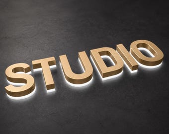 May include: A three-dimensional sign spelling the word STUDIO in capital letters. The letters have a metallic gold finish on the front and sides, with a bright white light glowing from the base of each letter, creating a halo effect on the surface.