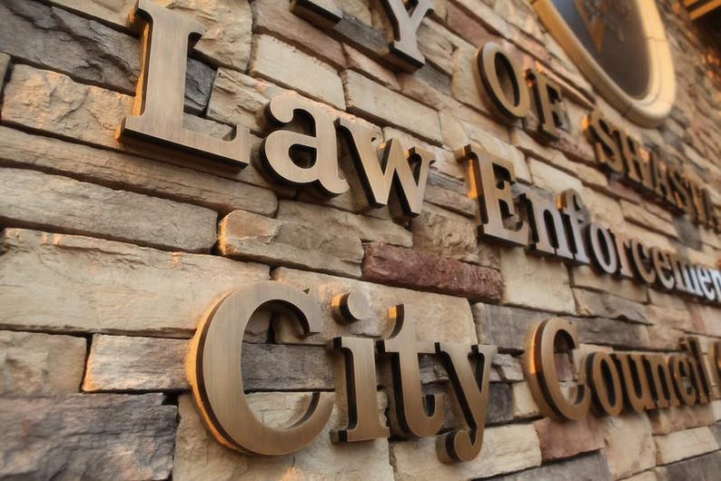 Puede incluir: Un muro de piedra con letras met&aacute;licas tridimensionales de color bronce que forman la inscripci&oacute;n City of Law Enforcement City Council. El muro est&aacute; construido con piedras rectangulares apiladas en tonos beige, gris y marr&oacute;n.