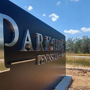 Puede incluir: Un letrero exterior grande, rectangular y de color negro mate con letras met&aacute;licas plateadas en relieve que forman la palabra PARKSIDE PENINSULA. El letrero est&aacute; montado sobre una base de hormig&oacute;n en un entorno exterior con hierba.