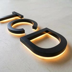 Puede incluir: Letras tridimensionales T, C y D con acabado en negro mate. Cada letra cuenta con una tira de luz LED blanca c&aacute;lida integrada a lo largo del borde inferior, creando un efecto brillante que ilumina la superficie bajo los caracteres.