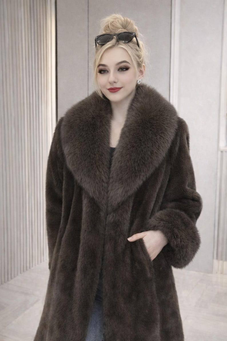 May include: A long, brown faux fur coat with a wide collar and cuffs. The coat has a classic design with a tailored fit and a pocket. The coat is a luxurious outerwear piece, perfect for cold weather.