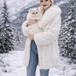 May include: A white faux fur coat with a matching hat and a fluffy white cat. The coat has a large collar and is worn with blue jeans and tan boots. The background features a snowy landscape with evergreen trees.