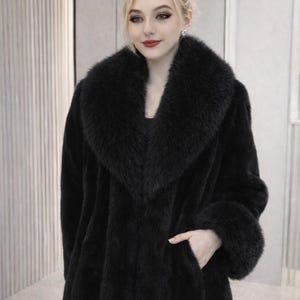 May include: A long, black faux fur coat with a wide collar and cuffs. The coat has a classic design with a tailored fit and a single pocket. The model is wearing sunglasses on top of their head.